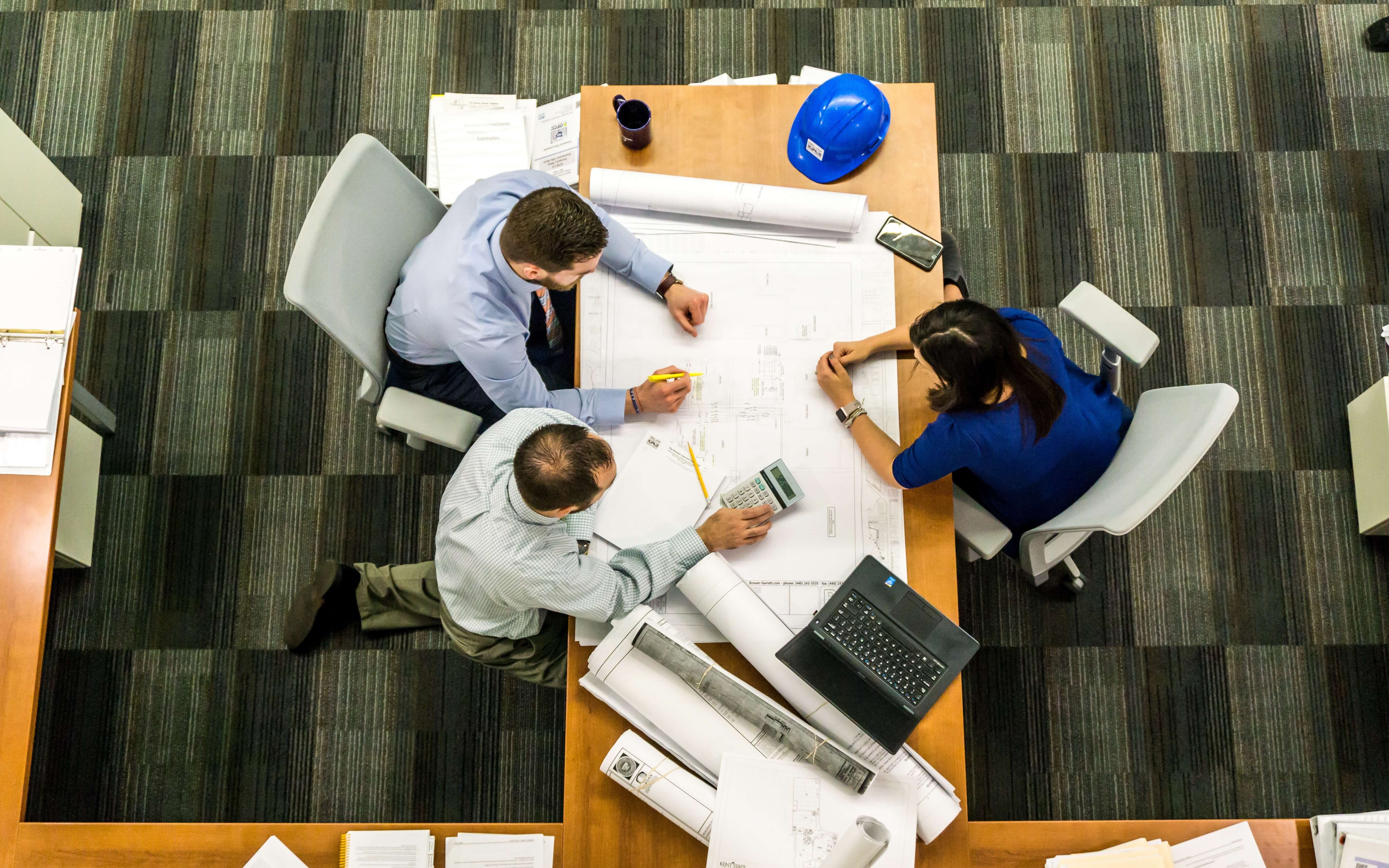 Three people meeting around a desk with drawings.